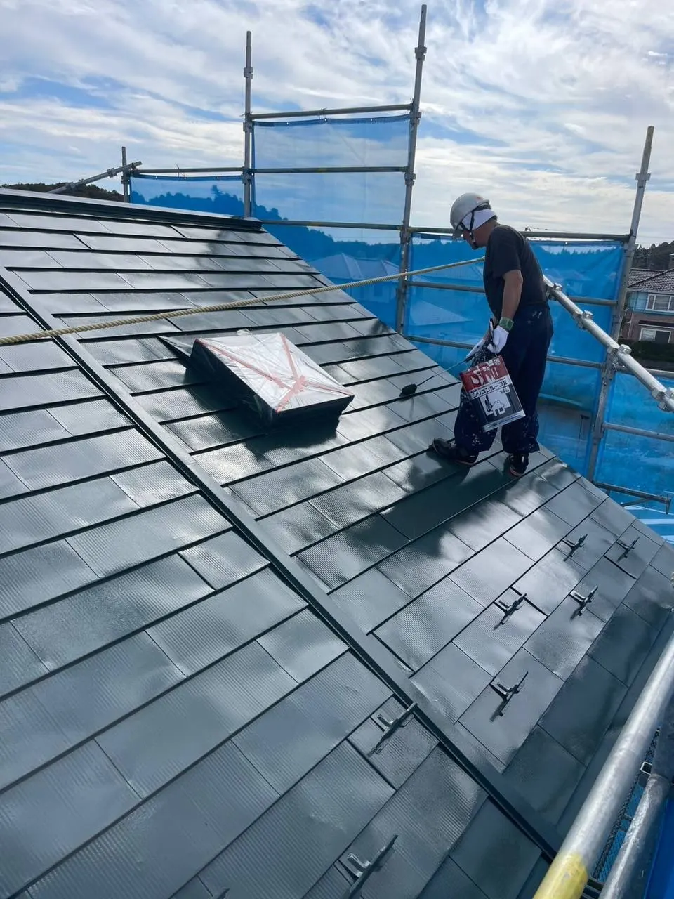 天窓のある屋根でローラーを使って塗装する職人